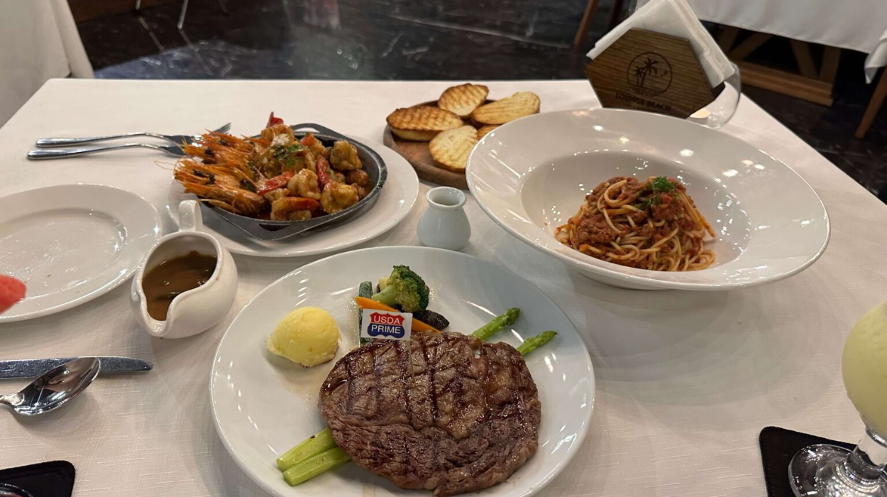 さまざまな料理(ステーキ、エビ、パスタ、パン)が並べられたテーブル。